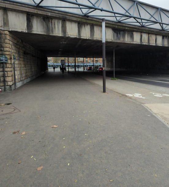 Passage sous le boulevard périphérique : large trottoir sombre sous l'ouvrage, piste cyclable sur le trottoir, tramway visible au fond