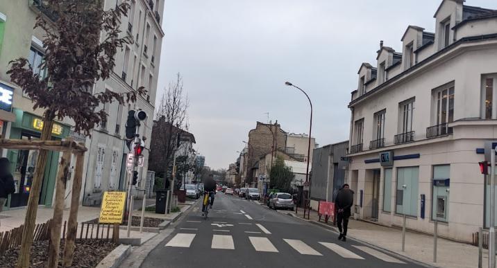 Rue Honoré-d'Estienne-d'Orves : rue commerçante étroite, passage piéton, cycliste sur la chaussée et stationnement des deux côtés